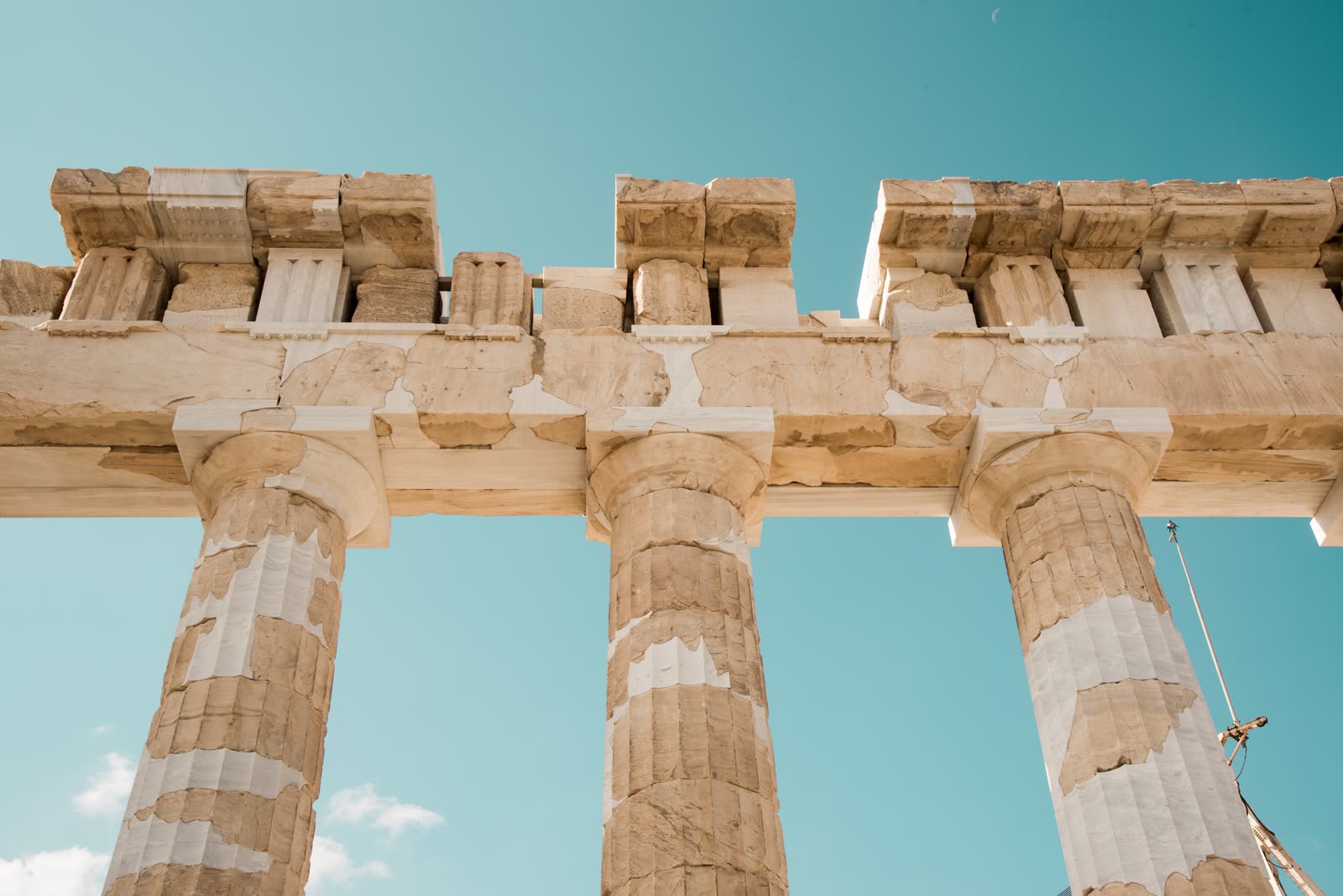 Three fluted marble Doric columns and their weathered entablature seen from below against a clear teal sky.